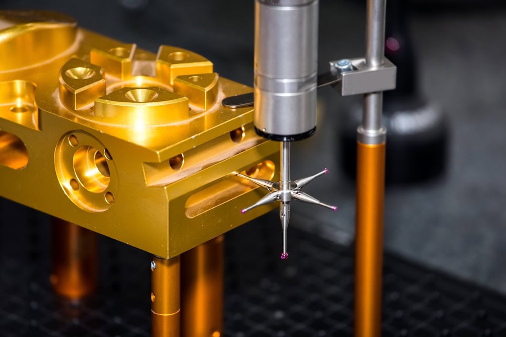 Gear measuring machine Close-up of a precision measurement tool with a metallic, multi-pronged probe positioned against a gold-colored mechanical component. The setup appears to be part of a laboratory or manufacturing inspection process.