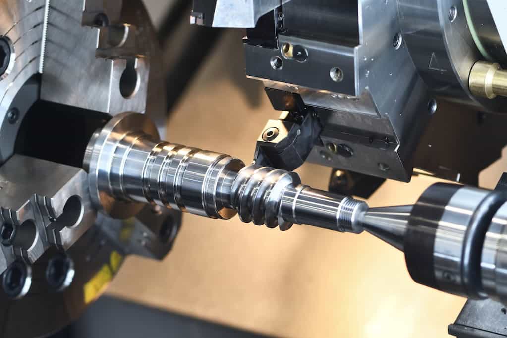 General purpose mounting solutions. A close-up of a CNC machine in operation, precisely cutting a metal workpiece with intricate grooves and a pointed end. The machine features various components and a rotating chuck, highlighted by gleaming metallic surfaces.