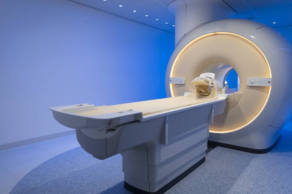 MRI scanner in hospital A white MRI machine in a modern medical setting is positioned in a clean, softly lit room. The table is extended, ready for a patient, beneath a circular scanner with soft ambient lighting.