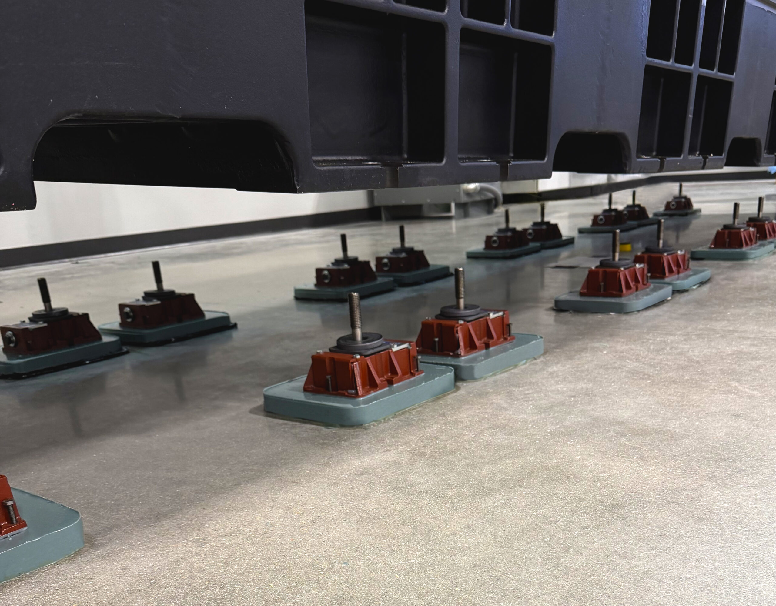 A large piece of industrial machinery suspended above multiple red and gray leveling mounts on a concrete floor.